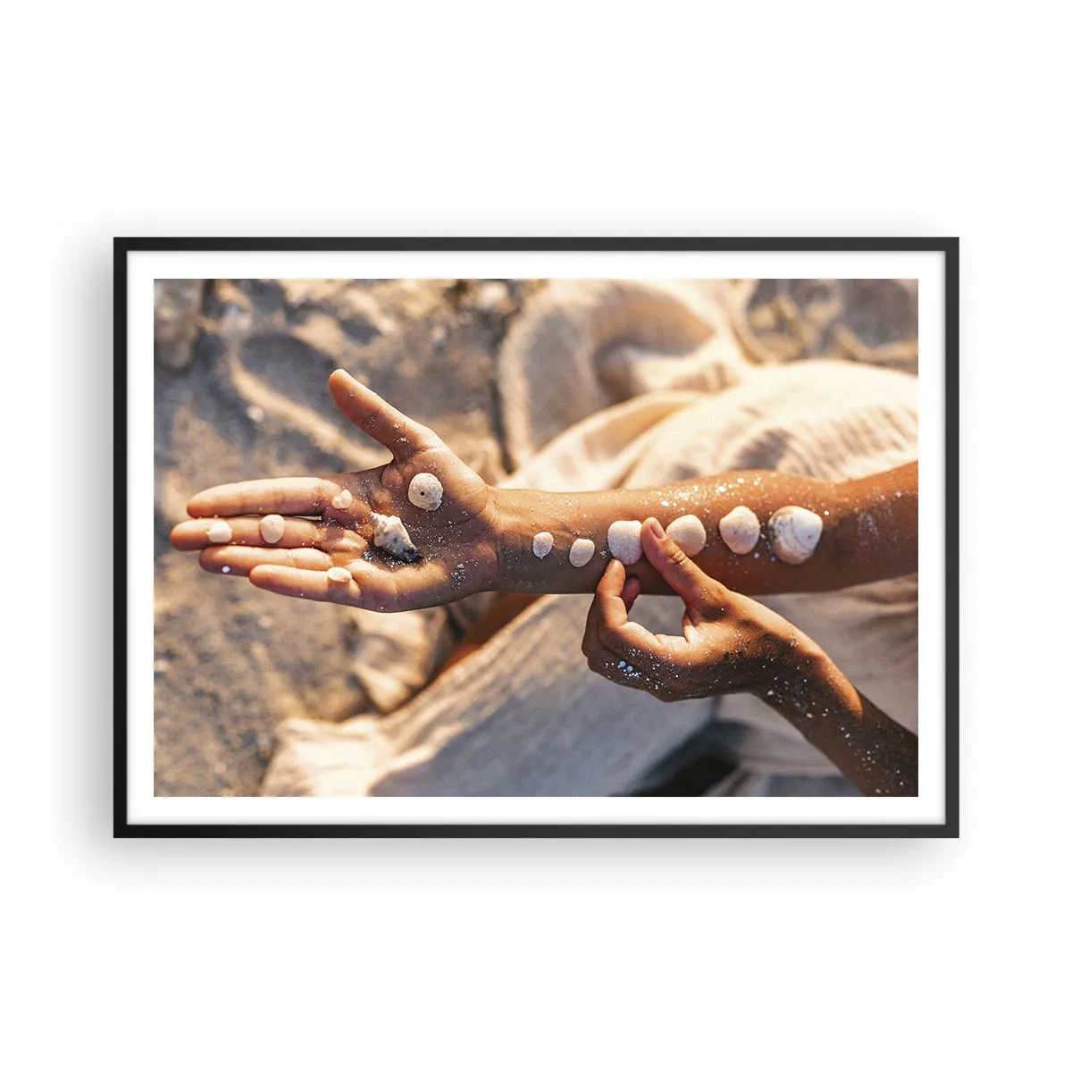 Póster en marco negro - Manos con conchas marinas dispuestas sobre el fondo de arena. - 100x70cm - La belleza al alcance de la mano - Decoración de pared moderna para salón y dormitorio ARTTOR